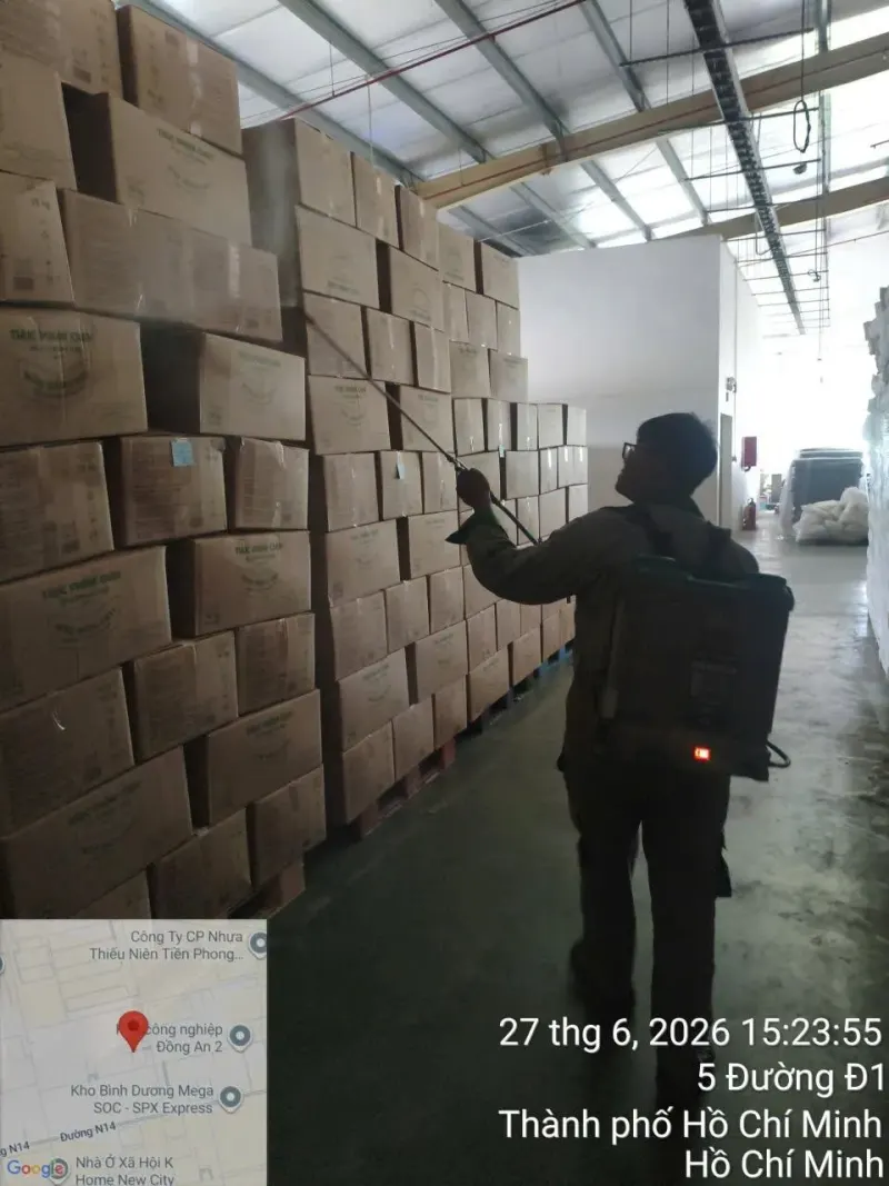 Kỹ thuật viên phun dọc lối đi giữa các chồng thùng carton trong kho