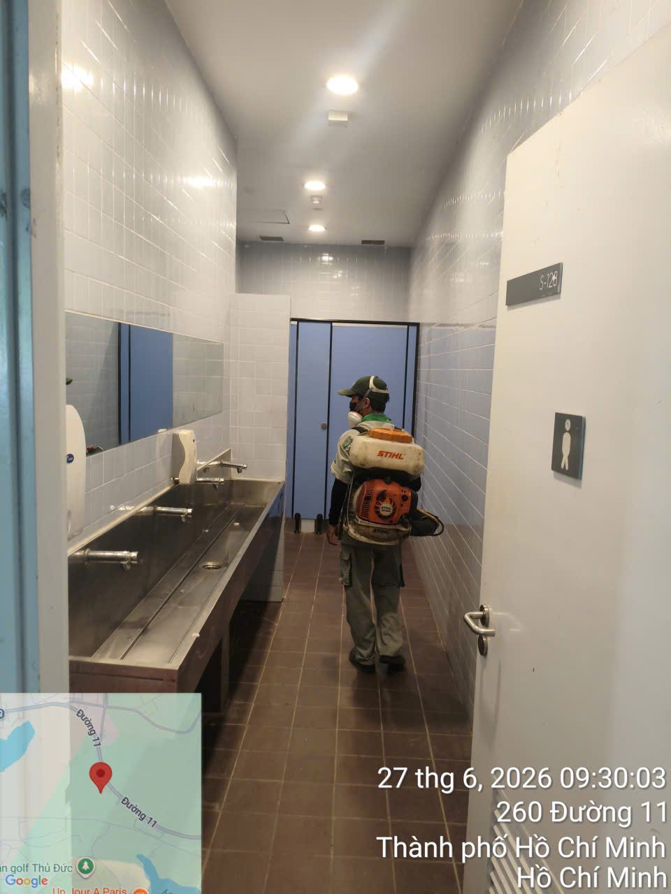 Kỹ thuật viên phun xử lý trong khu vệ sinh chung, dọc dãy bồn rửa