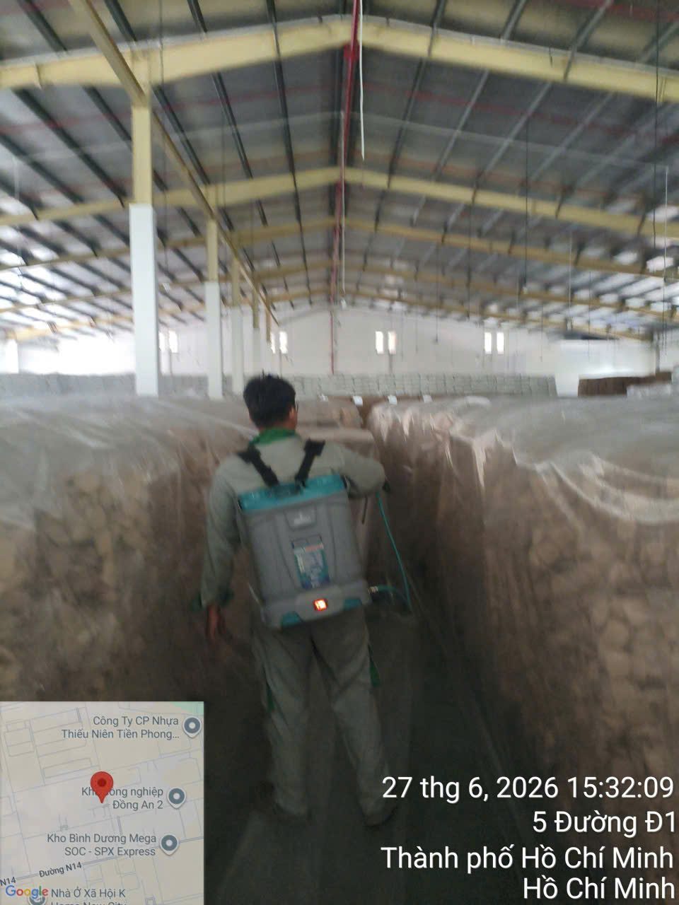 Kỹ thuật viên phun xử lý giữa hai dãy pallet hàng trong kho nhà máy