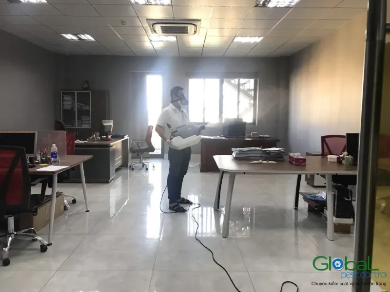 Kỹ thuật viên phun sương trong văn phòng có dãy bàn làm việc