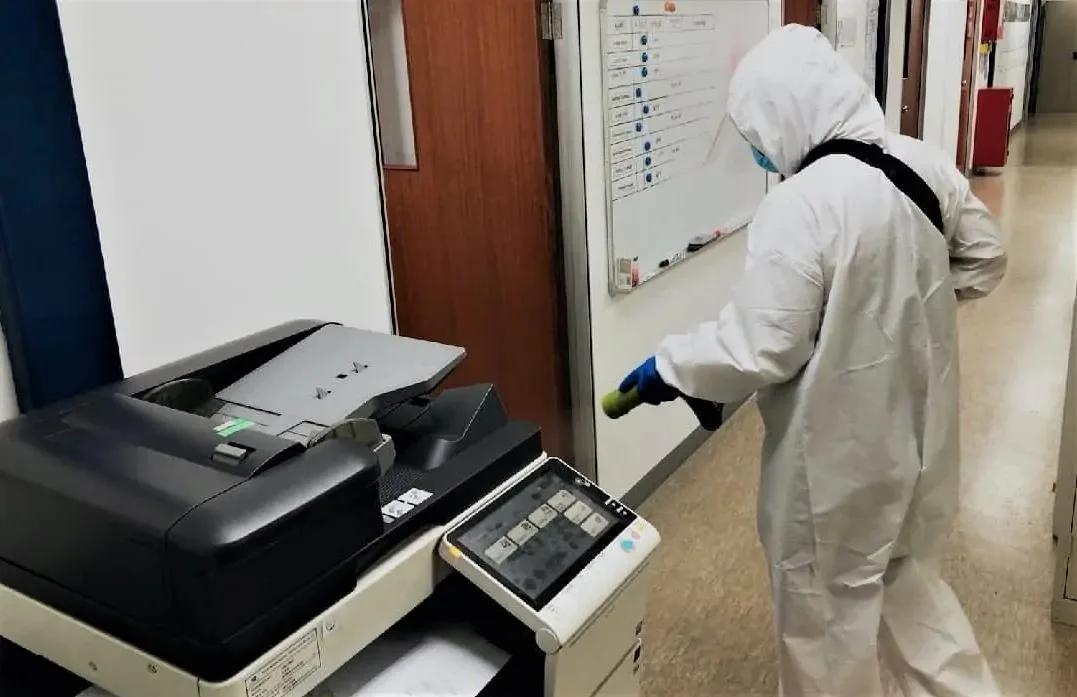 Kỹ thuật viên mặc đồ bảo hộ phun khử khuẩn quanh máy photocopy