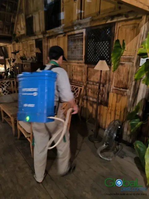 Kỹ thuật viên đeo bình phun điện xử lý côn trùng quán cà phê sân vườn