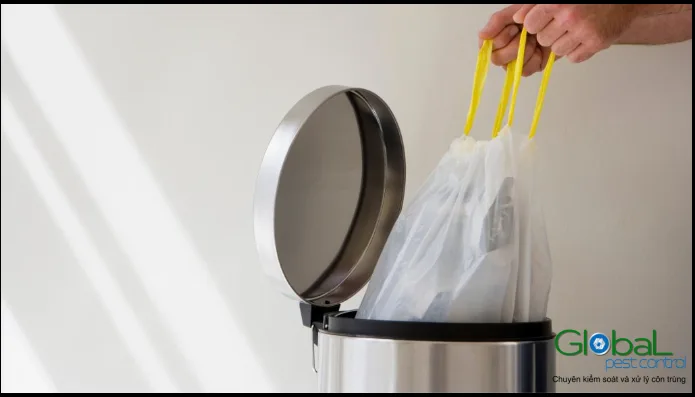Bàn tay nhấc túi rác trắng quai vàng ra khỏi thùng rác inox đạp chân