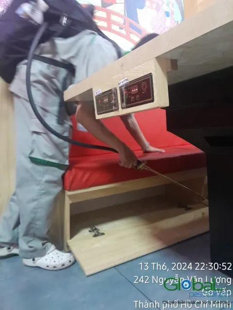 Kỹ thuật viên phun thuốc diệt gián kẽ ghế sofa đỏ trong nhà hàng