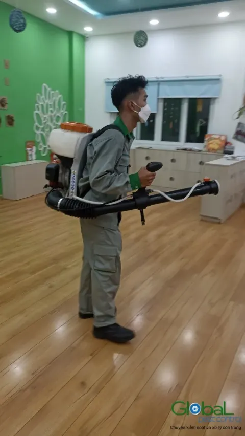 Kỹ thuật viên phun thuốc diệt côn trùng lớp học sàn gỗ trường mầm non