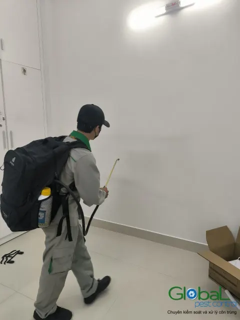 Kỹ thuật viên đeo bình phun xử lý côn trùng phòng trống mới sửa