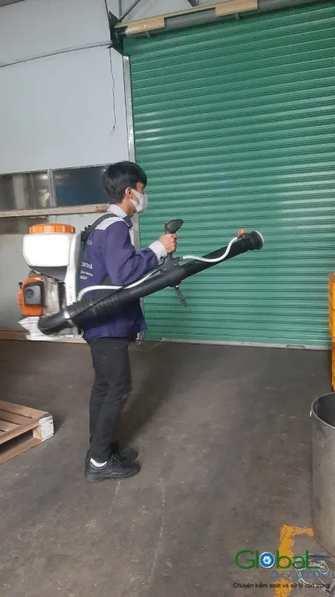 Kỹ thuật viên đeo máy phun động cơ phun thuốc khu cửa cuốn kho hàng
