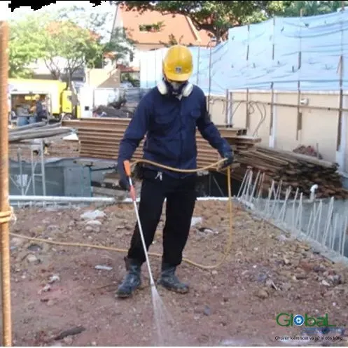 Công nhân đội mũ bảo hộ phun thuốc chống mối xuống nền móng công trình