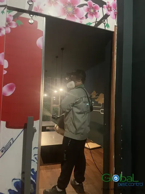 Kỹ thuật viên phun thuốc diệt côn trùng khu bàn ăn nhà hàng có tranh tường