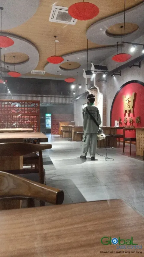 Kỹ thuật viên phun thuốc diệt côn trùng giữa dãy bàn ăn nhà hàng