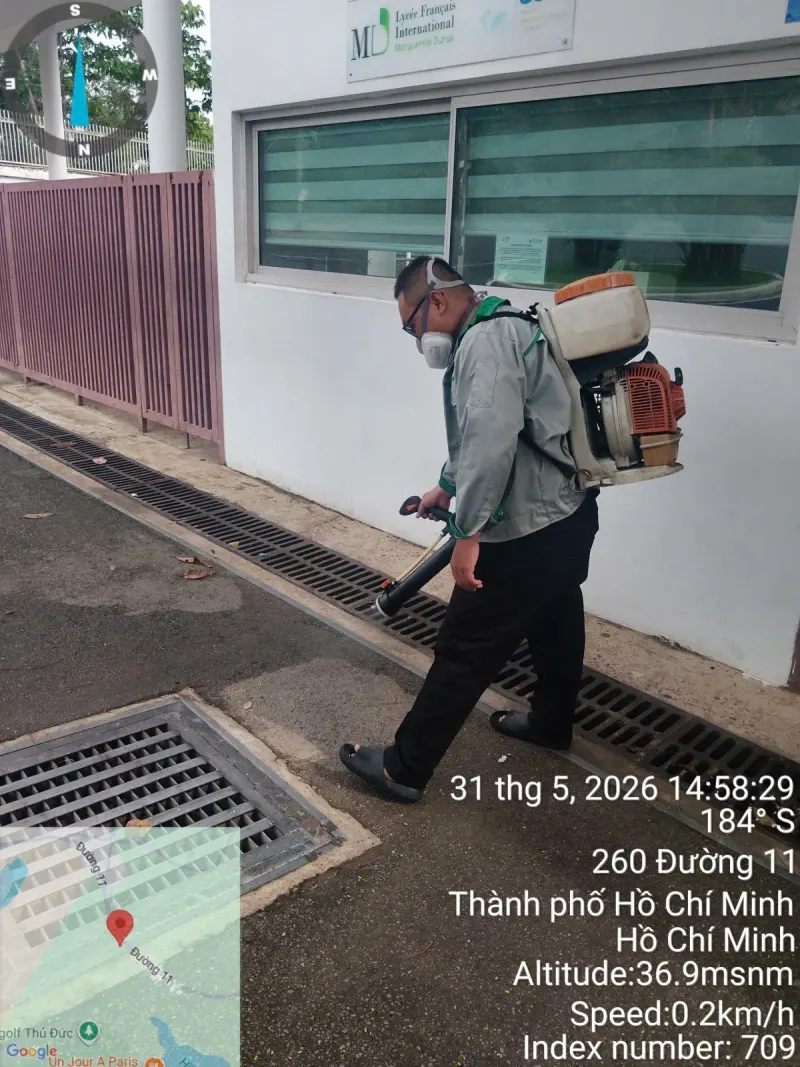 Kỹ thuật viên đeo máy phun động cơ phun thuốc dọc rãnh thoát nước ngoài nhà