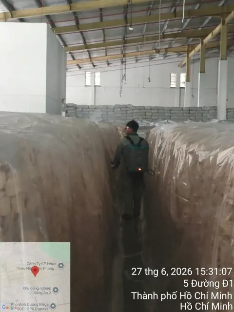 Kỹ thuật viên phun thuốc giữa các pallet hàng phủ bạt trong kho
