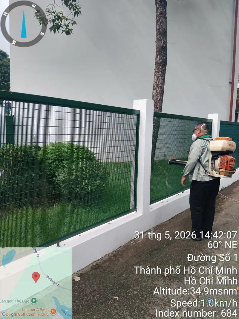 Kỹ thuật viên phun thuốc diệt muỗi dọc hàng rào sân trường