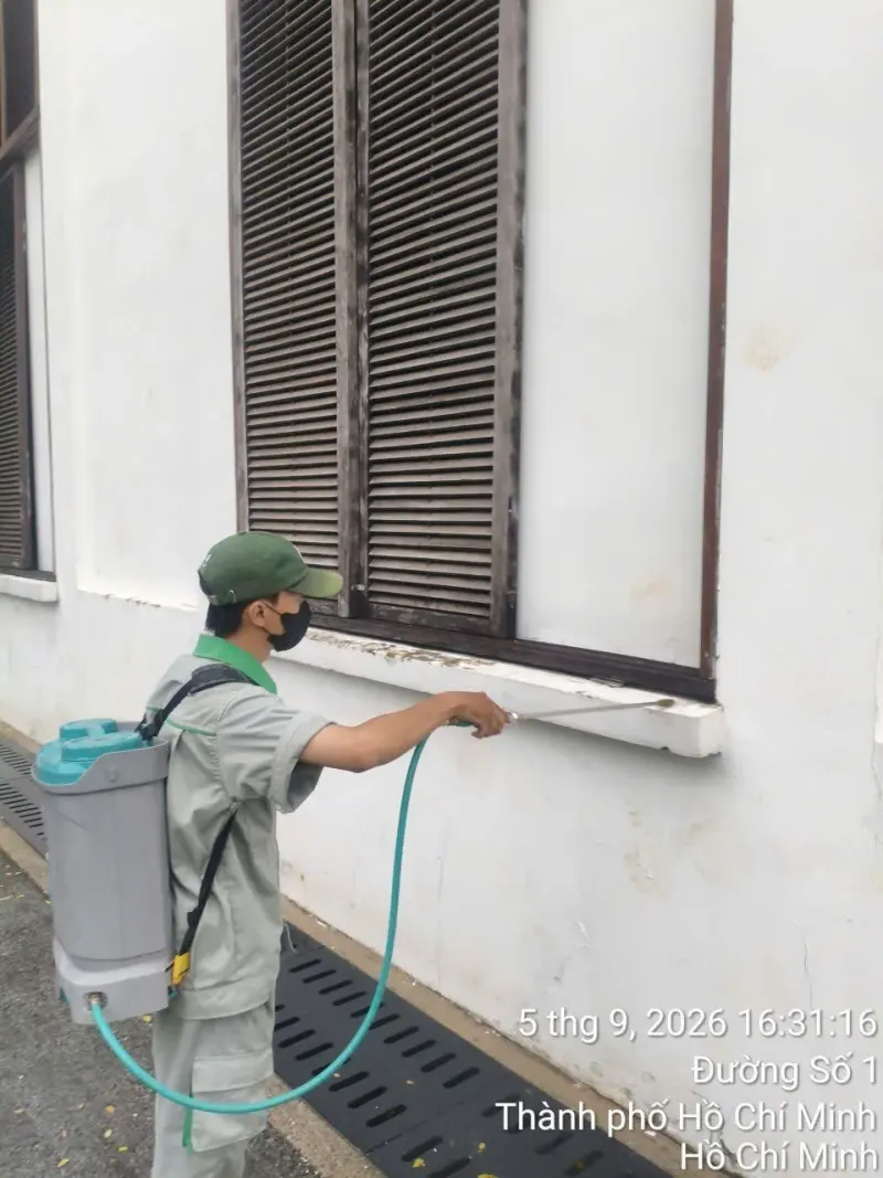 Kỹ thuật viên đeo bình phun xịt dung dịch lên bậu cửa sổ và tường ngoài có vệt ố, sát rãnh thoát nước