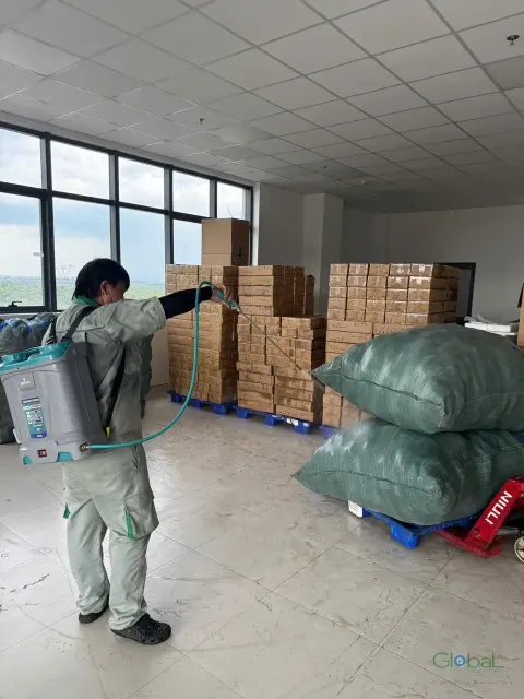 Kỹ thuật viên phun thuốc quanh hàng hoá phủ bạt trong kho