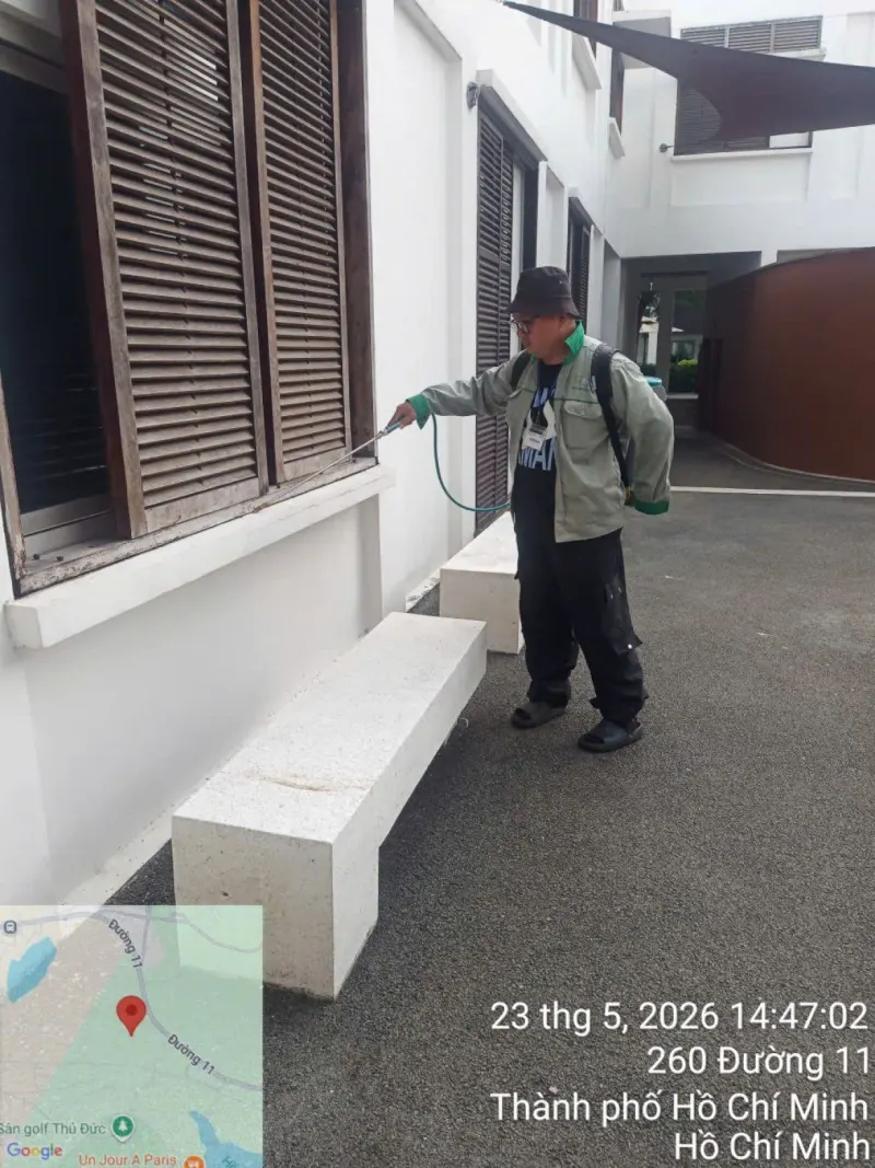 Kỹ thuật viên phun dọc chân tường và cửa chớp mặt ngoài một căn nhà