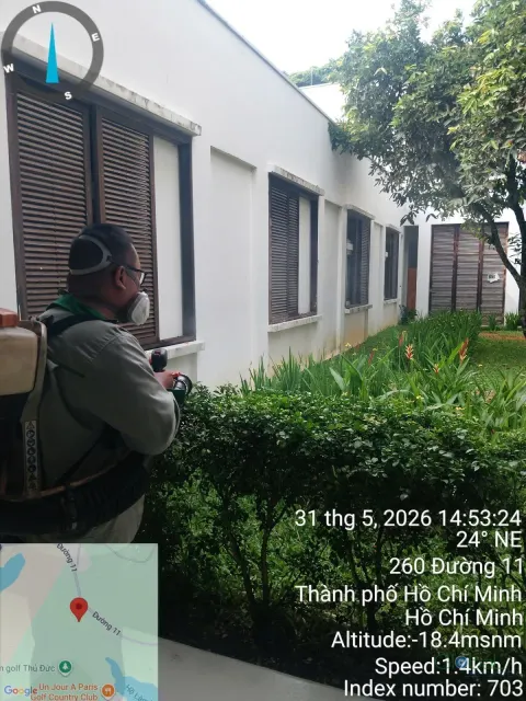 Kỹ thuật viên phun thuốc diệt muỗi bụi cây sát dãy nhà trường học