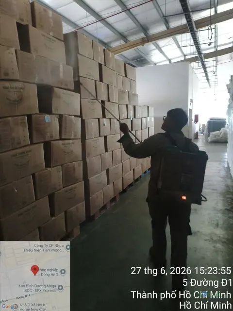 Kỹ thuật viên phun thuốc dọc kệ thùng carton trong kho tối