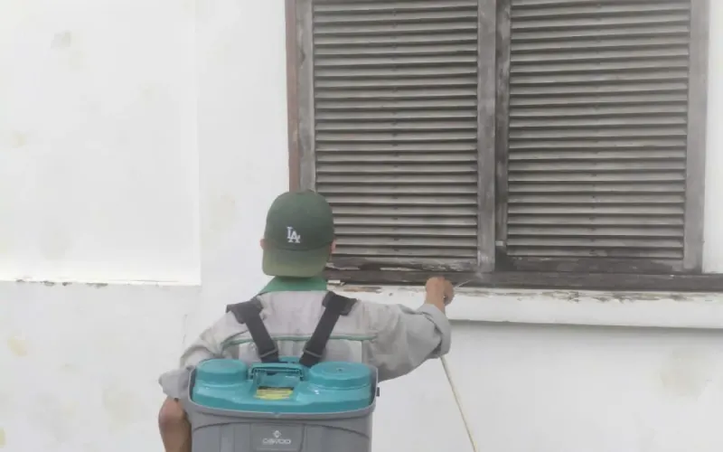 Kỹ thuật viên đeo bình phun xử lý quanh chân tường và cửa sổ tầng trệt của nhà ở