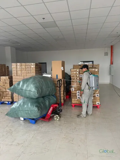Kỹ thuật viên phun thuốc khu hàng hoá trên pallet trong kho sáng