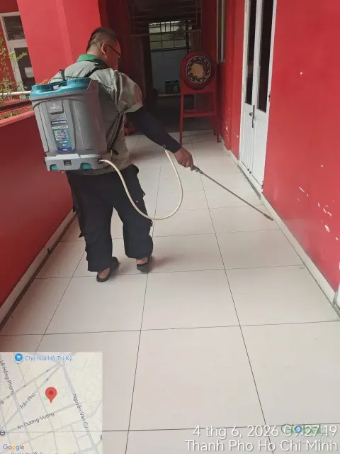Kỹ thuật viên đeo bình phun điện phun thuốc hành lang lớp học tường đỏ
