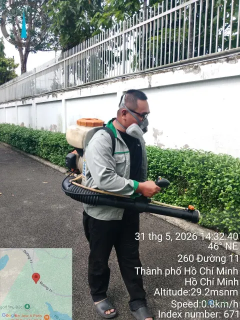 Kỹ thuật viên phun thuốc diệt muỗi dọc bồn cây sát tường rào trường