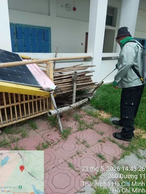 Kỹ thuật viên phun thuốc diệt muỗi cạnh đống vật liệu gỗ ngoài trời