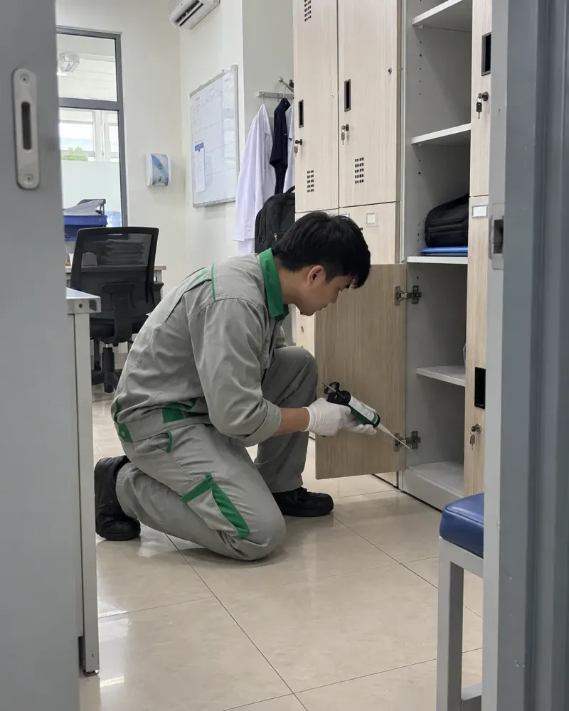 Kỹ thuật viên bơm gel diệt gián vào khe tủ phòng nhân viên phòng khám