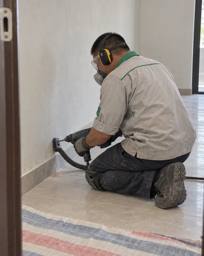 Kỹ thuật viên khoan chân tường nhà xử lý mối, đeo bảo hộ tai