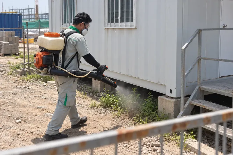 Kỹ thuật viên đeo máy phun động cơ phun chân vách và gầm lán container ở công trường