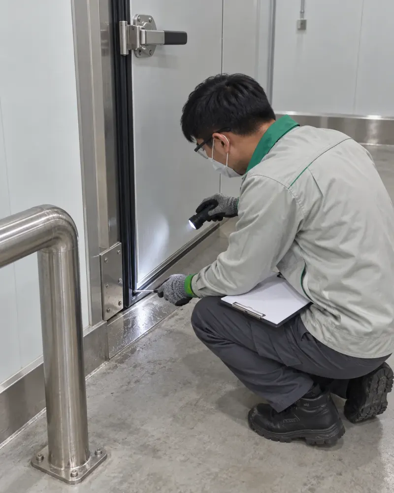 Kỹ thuật viên kiểm tra gioăng cửa kho lạnh, tay cầm bảng ghi