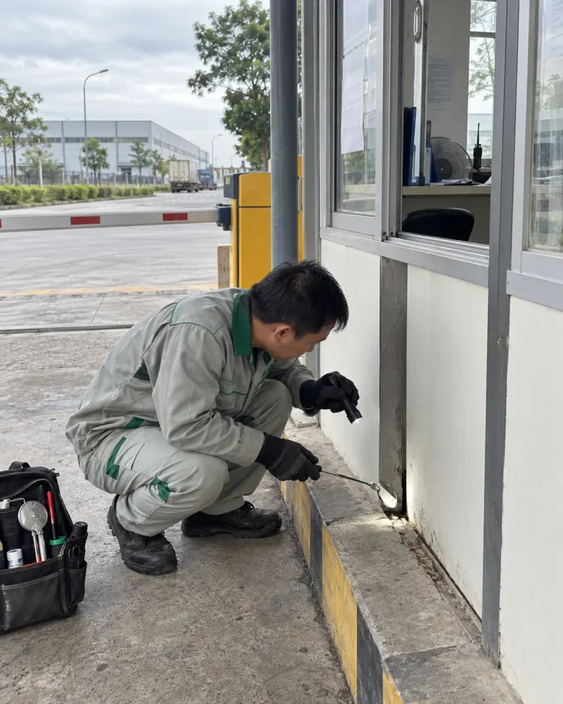 Kỹ thuật viên soi đèn pin khe chân tường nhà bảo vệ khu công nghiệp