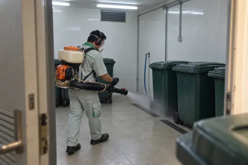 Kỹ thuật viên phun sương phòng rác tòa nhà có thùng rác xanh