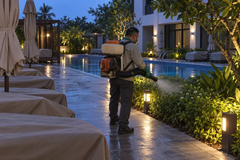 Kỹ thuật viên phun sương sân hồ bơi sau giờ đóng cửa, ghế nằm phủ bạt