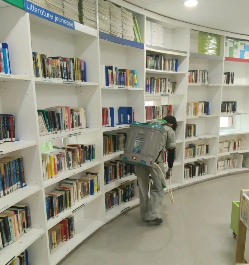 Kỹ thuật viên phun chân dãy kệ sách cong trong thư viện